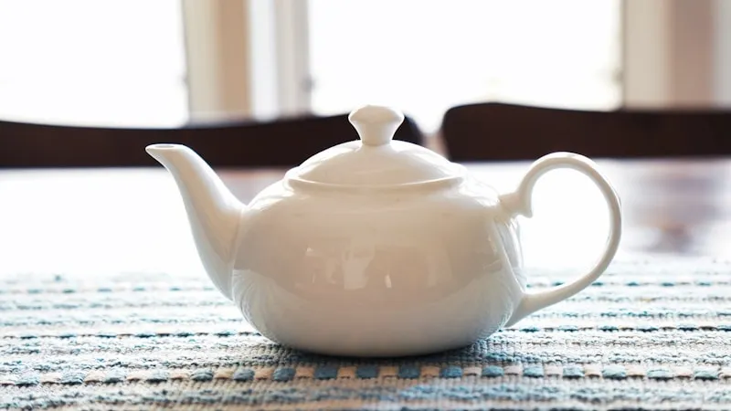A white teapot resting on a wooden table